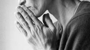 Mature woman in profile with hands clasped in prayer (cropped and black and white)