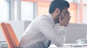 Man with head in his hands sat at his desk